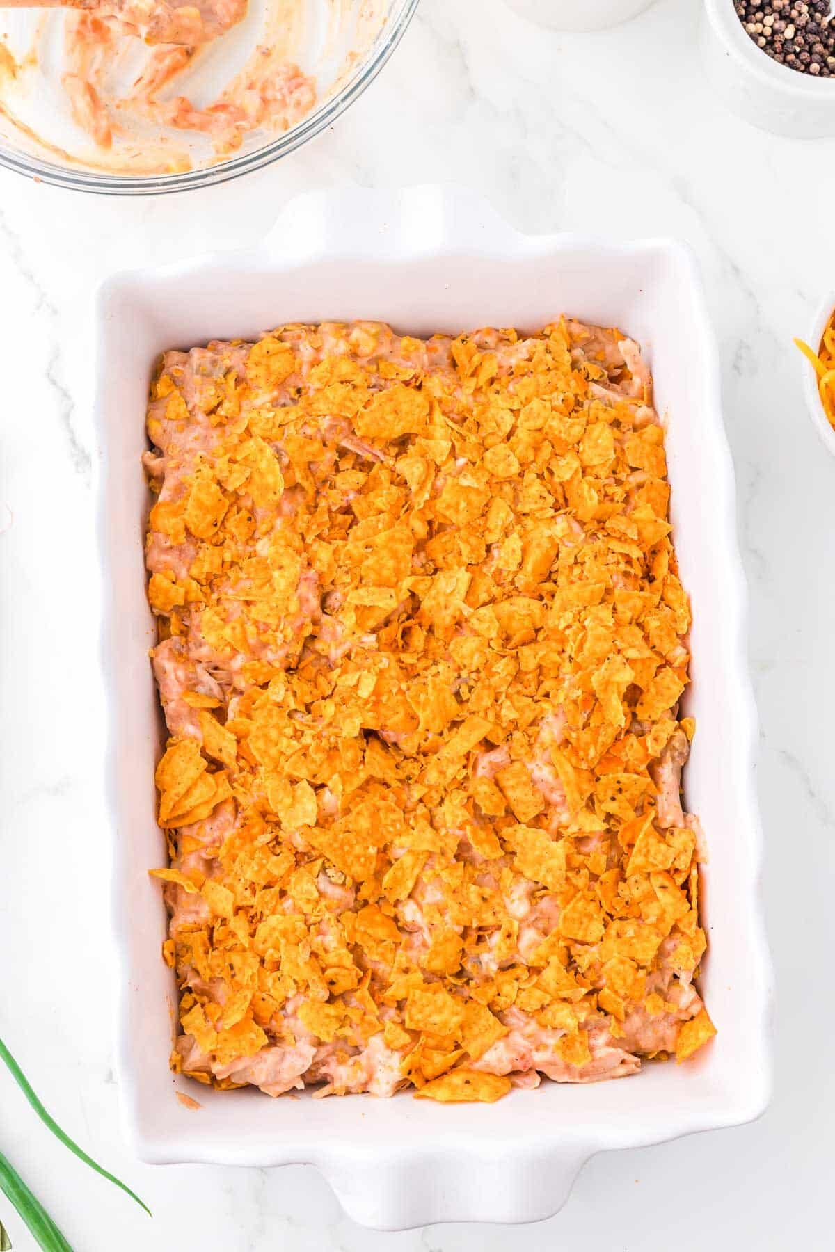 Mexican Chicken Casserole with Doritos being layered in a white casserole dish.
