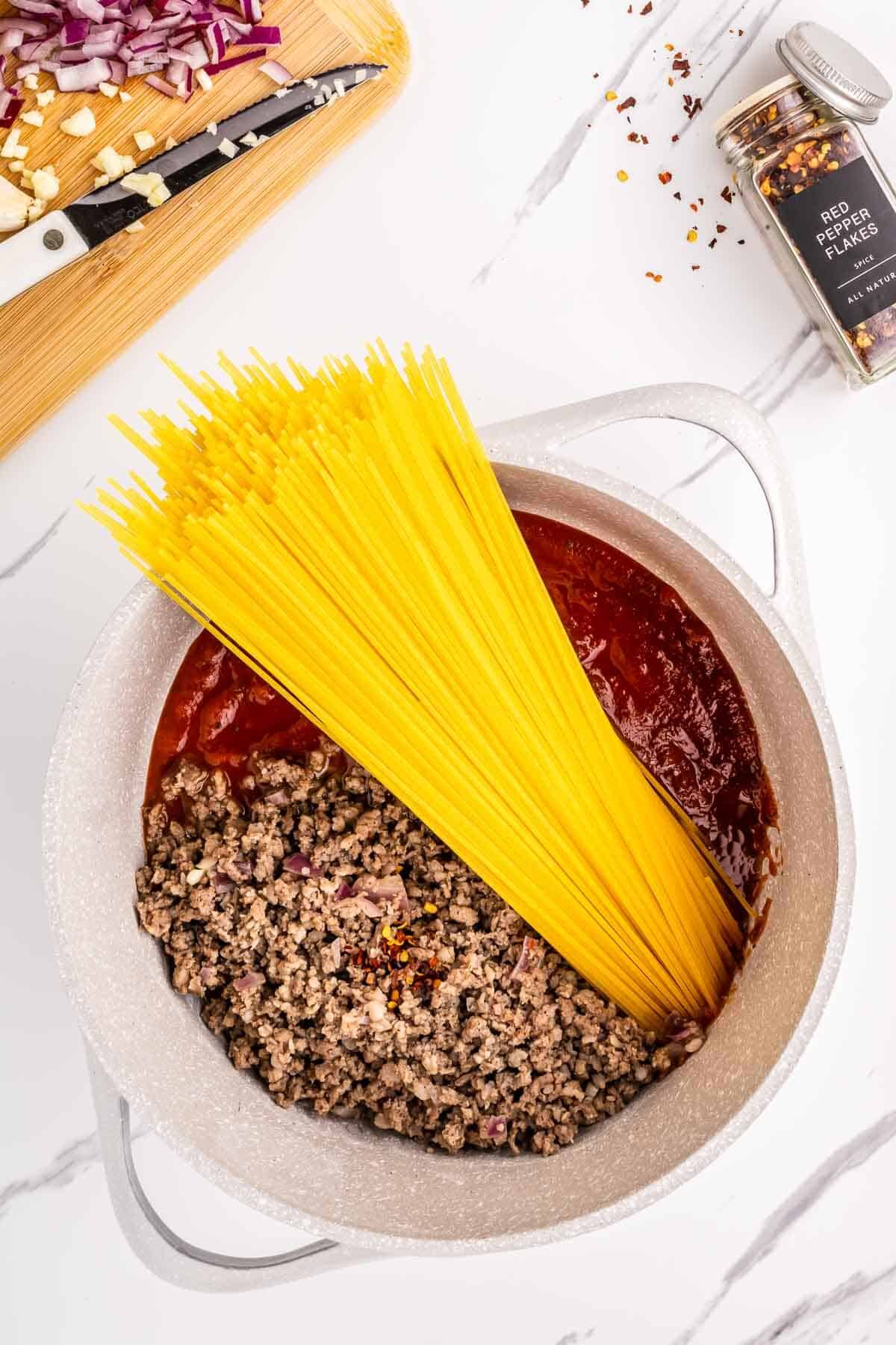 Spaghetti, broth and marinara sauce being added to the pot. 