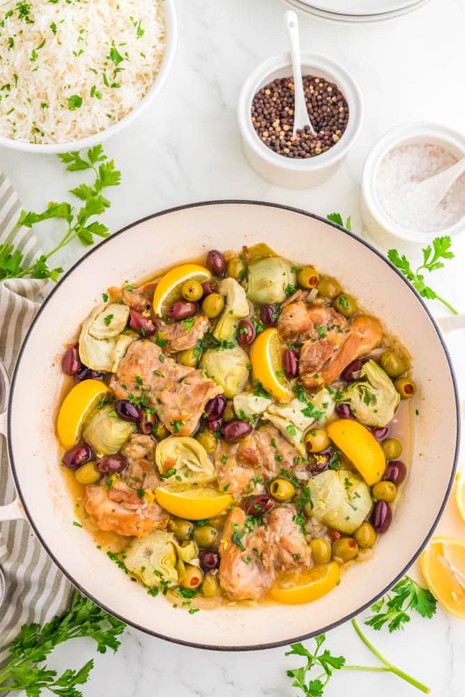 Greek chicken thighs in a pan with olives, lemons and artichoke hearts.