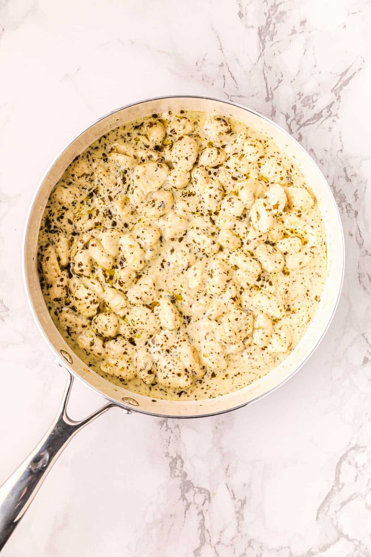 Creamy pesto gnocchi in a skillet cooking before cheese and lemon are added.
