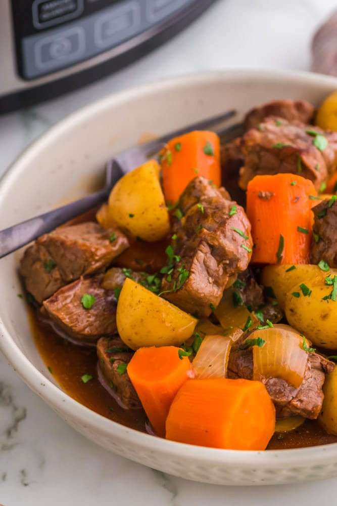 A bowl of Slow Cooker Irish Stew with a spoon and a crockpot in the background.