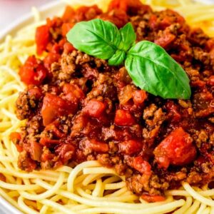 ground beef spaghetti sauce on a white plate garnished with fresh basil