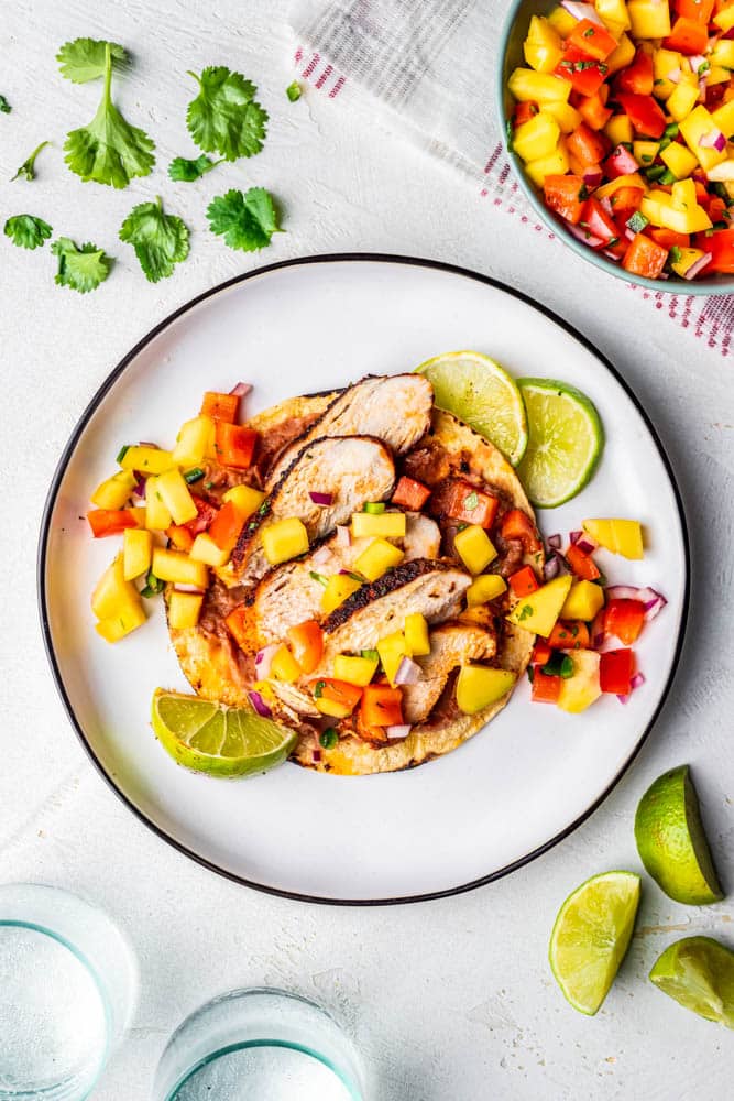 One blackened chicken taco on a white plate with refried beans and mango salsa.