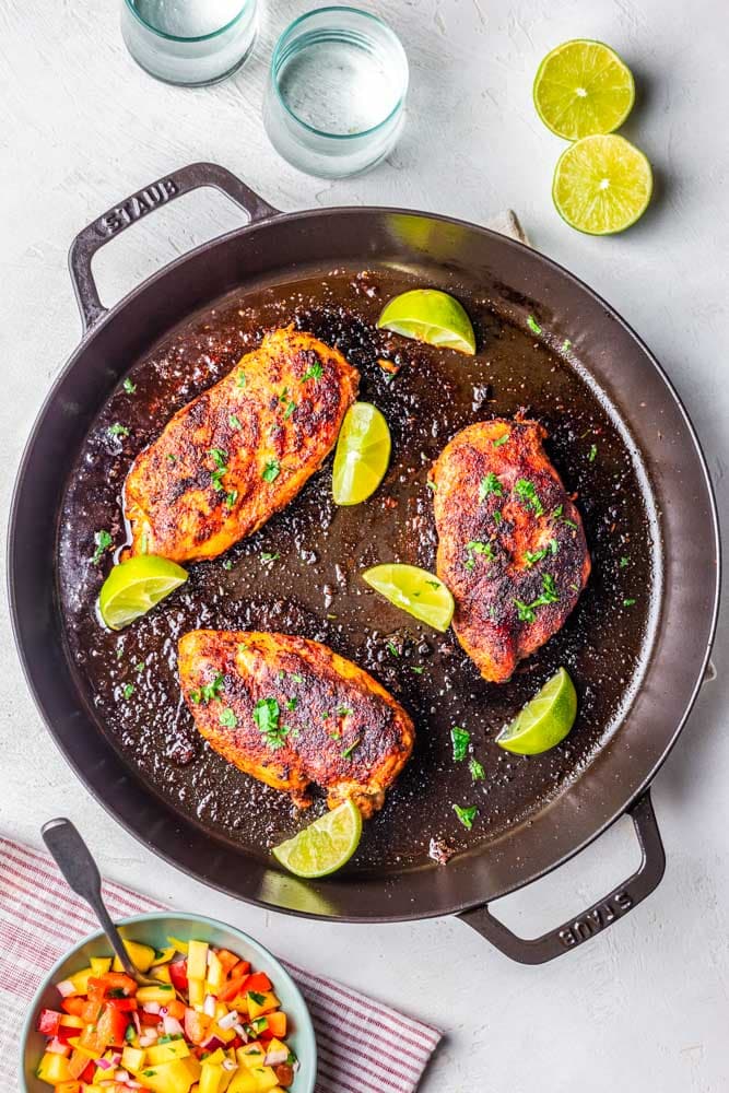Blackened chicken breasts in a cast iron skillet with lime.