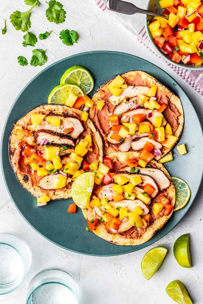 Blackened chicken tacos with mango salad on a plate with limes.