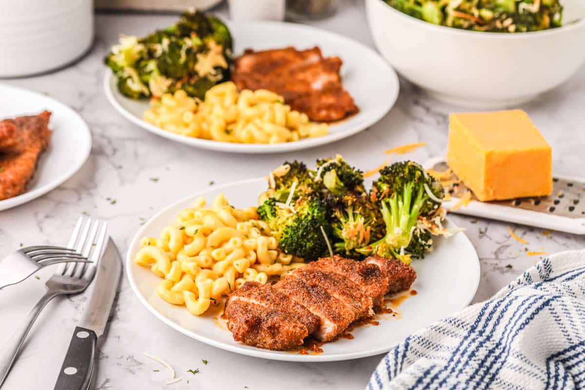  A white plate with pork chop baked from frozen, mac and cheese and broccoli.