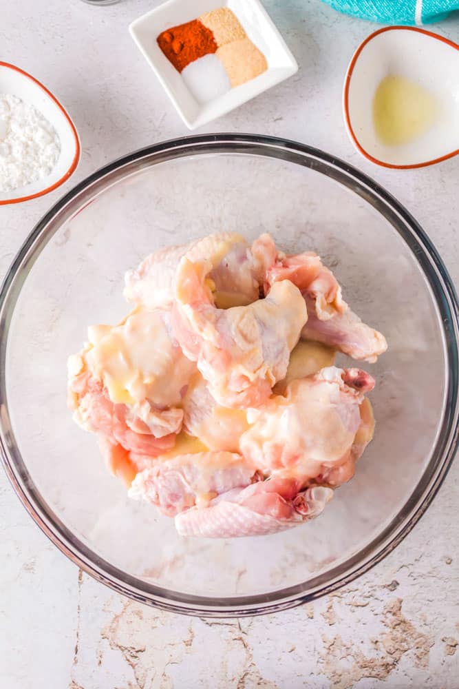 Raw chicken wings in a bowl with melted butter over the top.