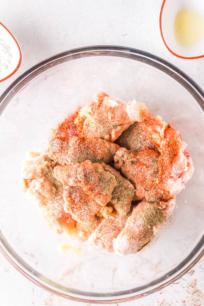 Raw chicken wings in a glass bowl with cornstarch and seasonings. 