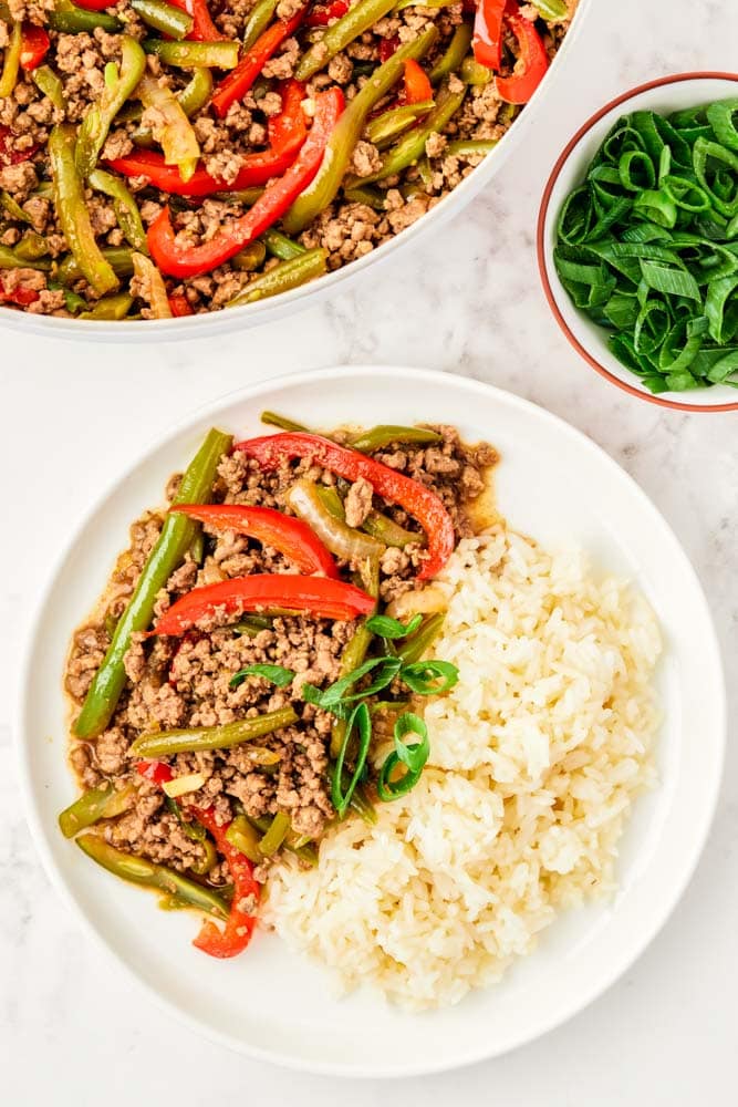 Ground beef stir fry with veggies on a white plate with rice.