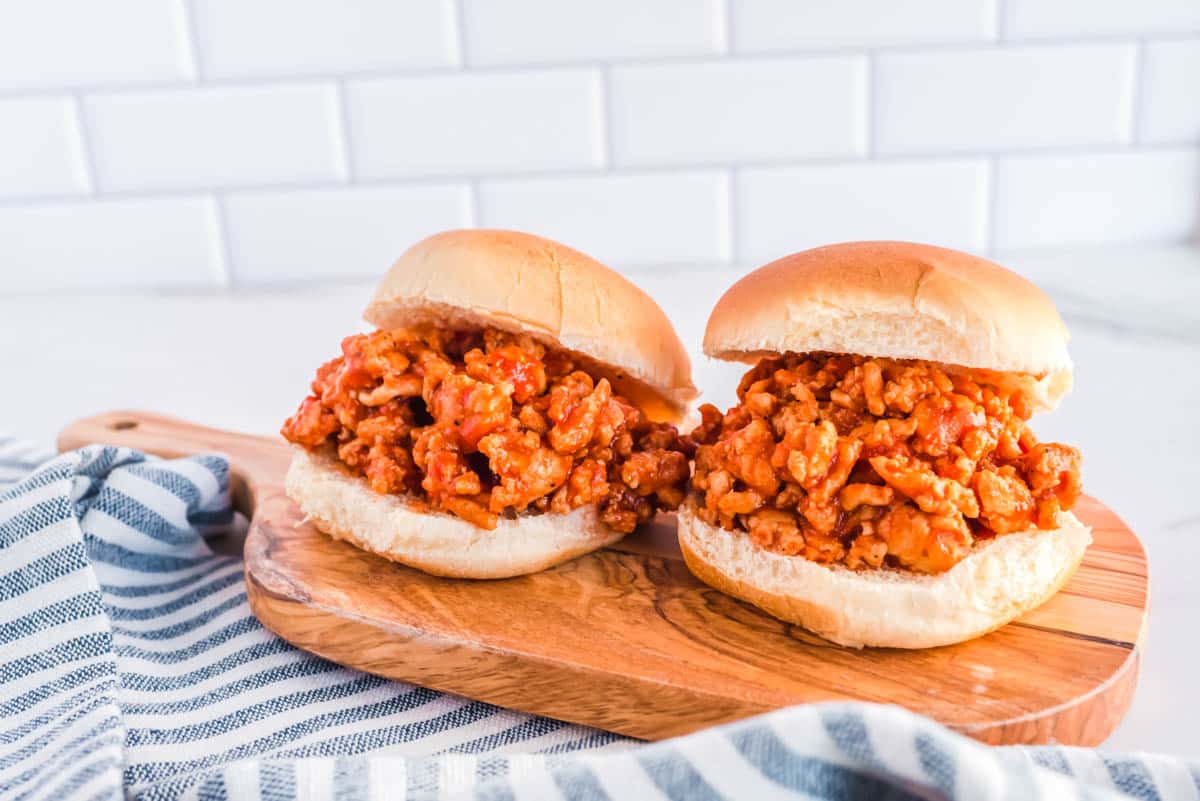 Two ground chicken sloppy joes on a cutting board with a blue striped cloth.