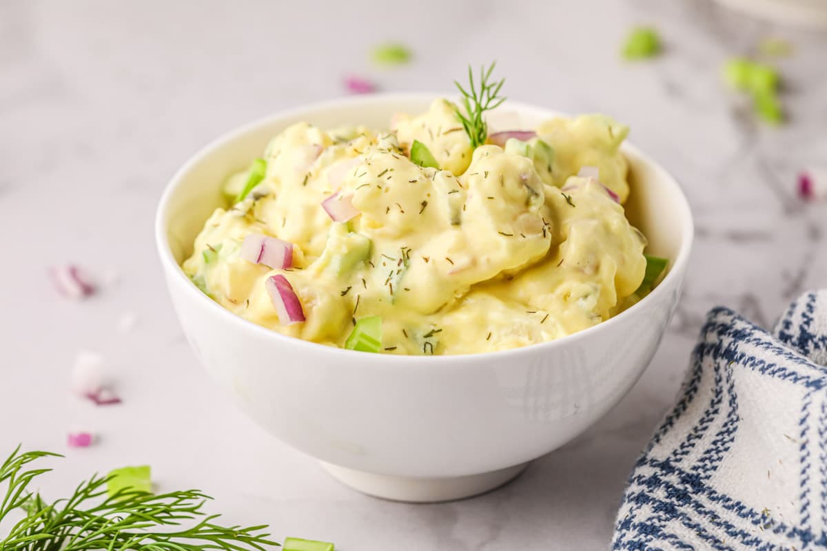 Creamy Potato Salad without Eggs in a small white bowl sprinkled with dill.