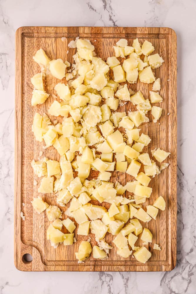 Potatoes being chopped into small cubes on a cutting board.