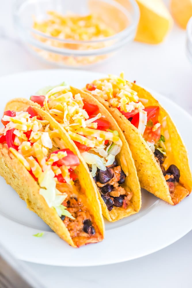 Three ground chicken tacos with taco toppings on a white plate.