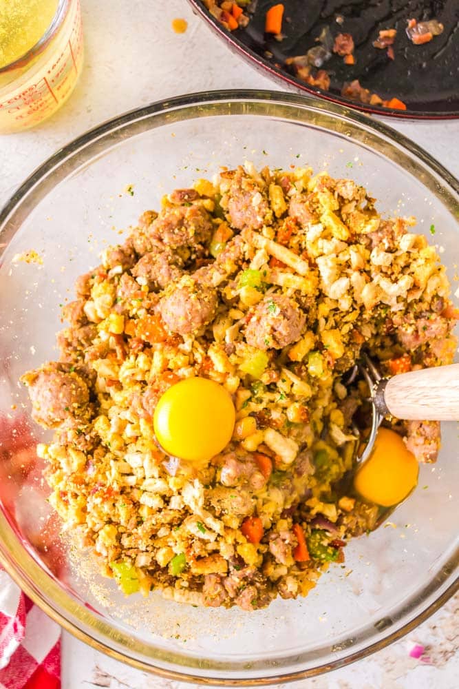 Eggs added to the sausage stuffing in a glass bowl.