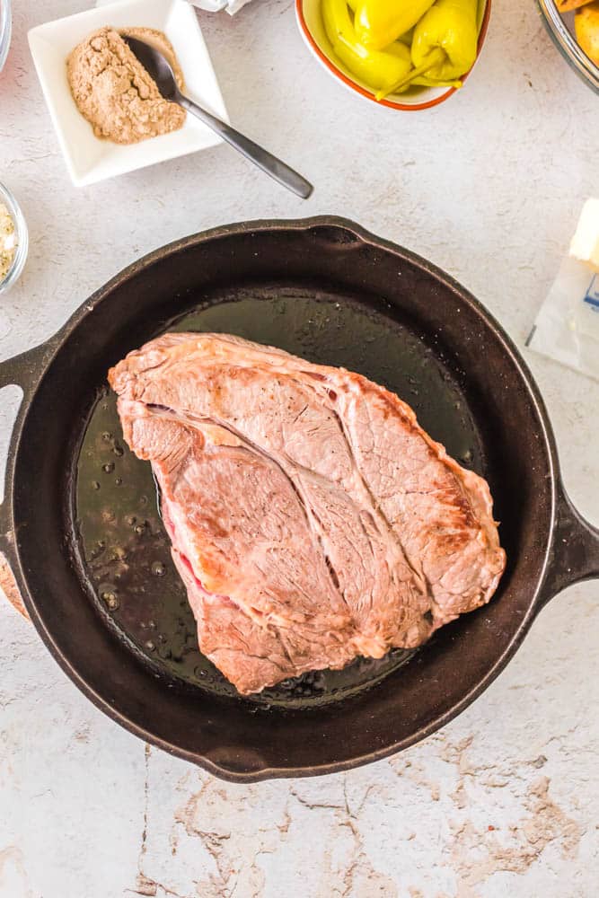 Chuck roast being seared in a cast iron skillet.