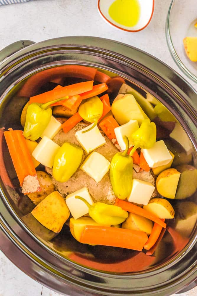 Veggies, butter and seasoning added to the chuck roast to make Mississippi Pot Roast with Potatoes and Carrots in the crockpot.