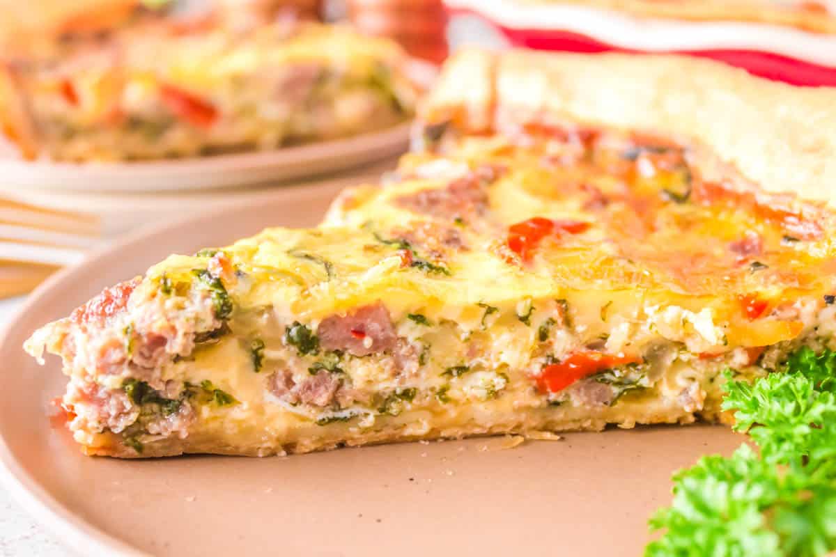 One piece of sausage and spinach Quiche on a plate.