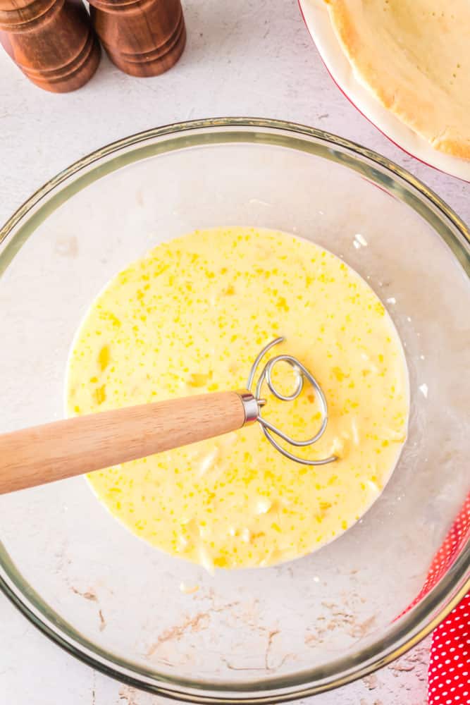 Eggs and cheese being stirred together in a glass bowl.