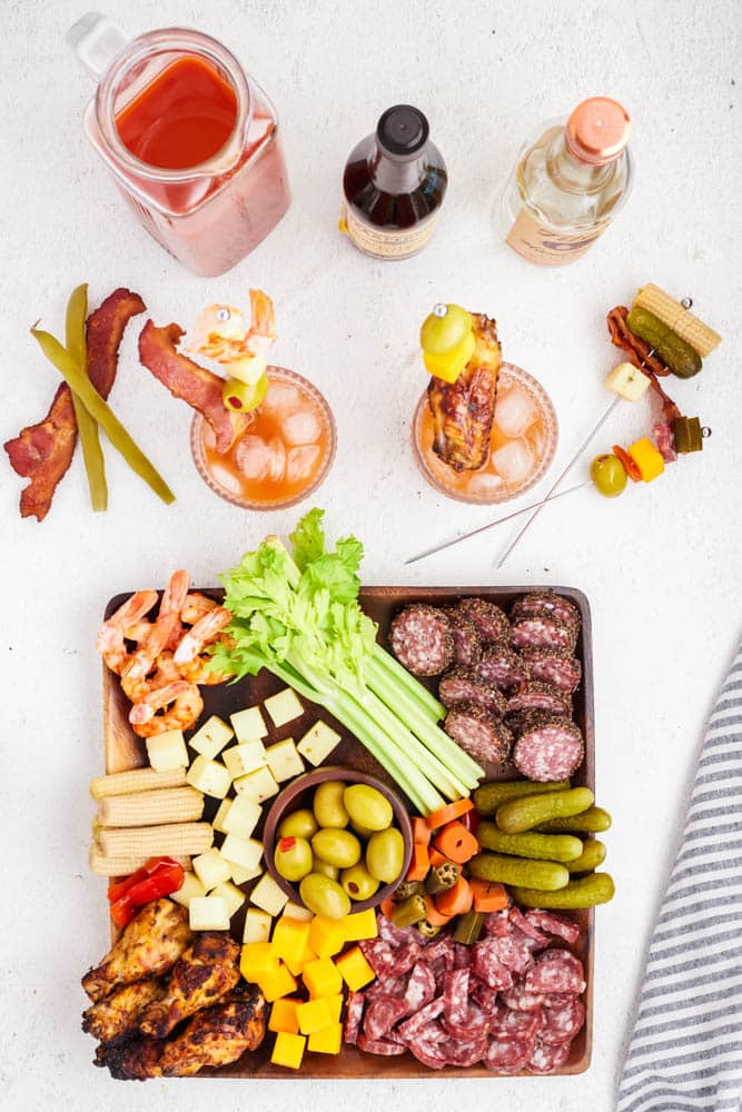 Lots of bloody mary garnishes on a large wooden charcuterie board.