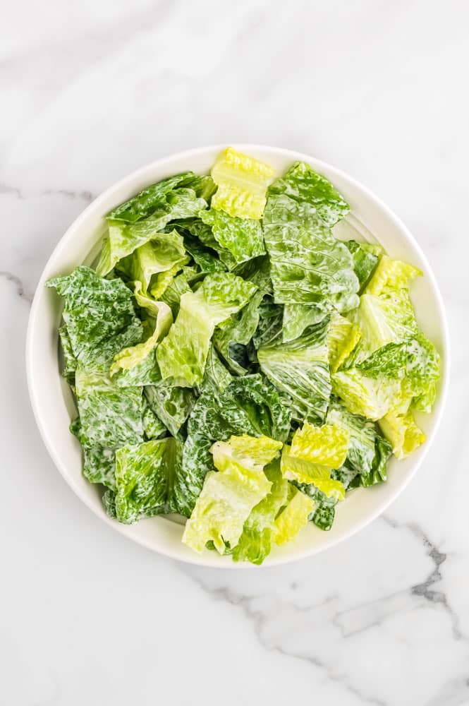 Romaine lettuce in a bowl tossed with Caesar dressing. 