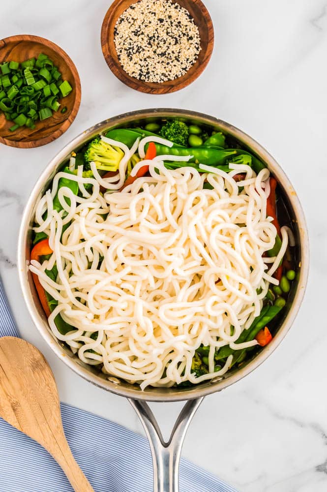 Udon noodles being added to a pan with veggies.