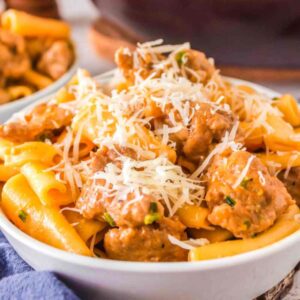 closeup of spicy italian sausage pasta in a white bowl with shaved parmesan on top