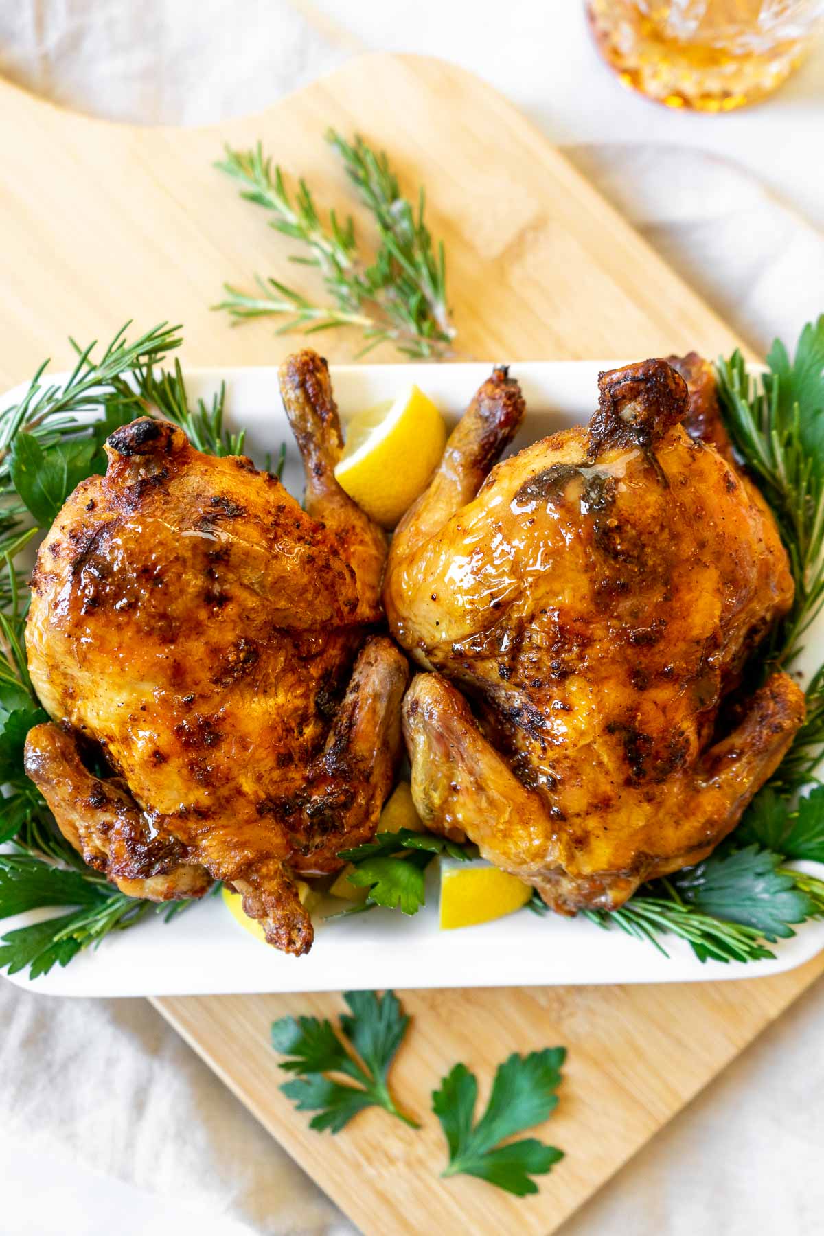 Two air fryer Cornish hens on a platter with rosemary and lemon