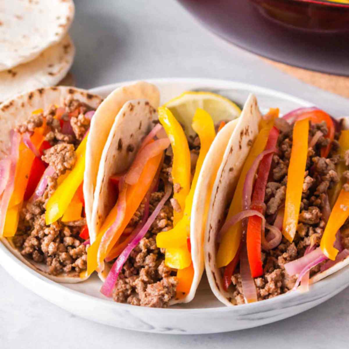 3 ground beef fajitas topped with onions and peppers in a white marble serving dish