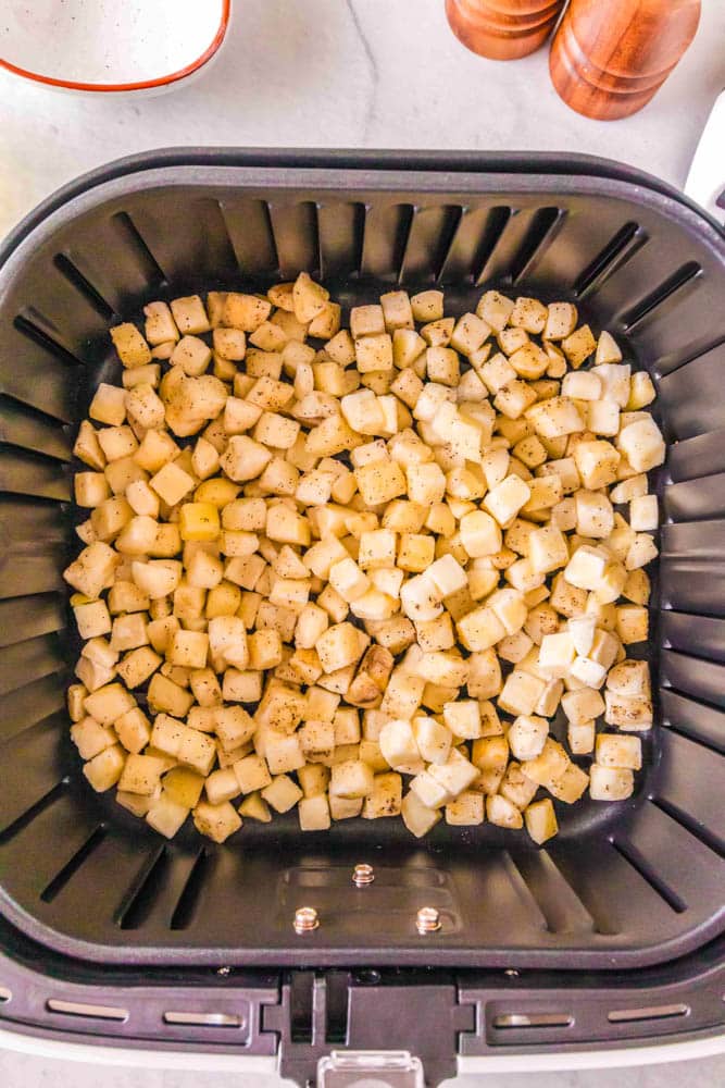 Diced hash browns in the air fryer before being cooked.