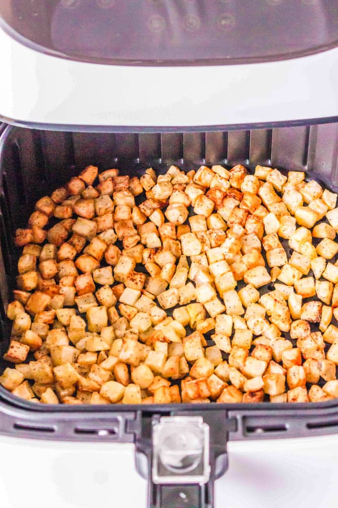 Diced hash browns in an air fryer basket after being cooked.