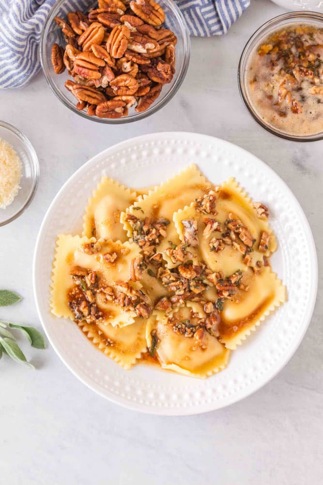 A plate of ravioli topped with a sage brown butter sauce and pecans.