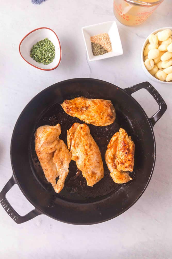 Four chicken breasts cooking in a cast iron skillet.