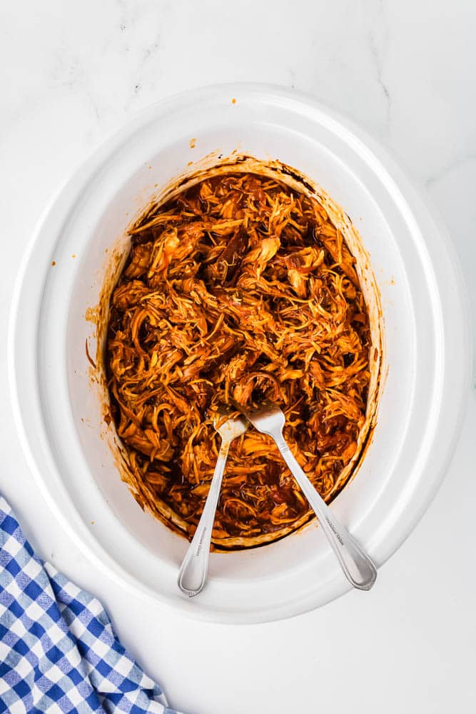Crockpot Pulled Chicken in the slow cooker being shredded with two forks.