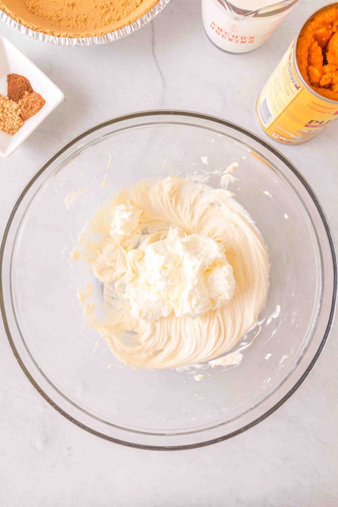 Cream cheese being whipped with a mixer in a glass bowl.