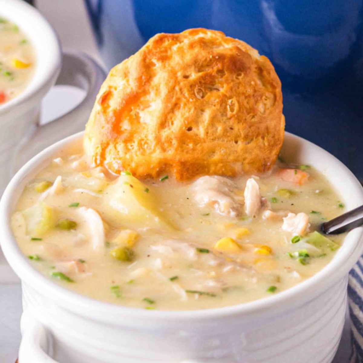 Chicken pot pie soup in a white bowl with a biscuit.