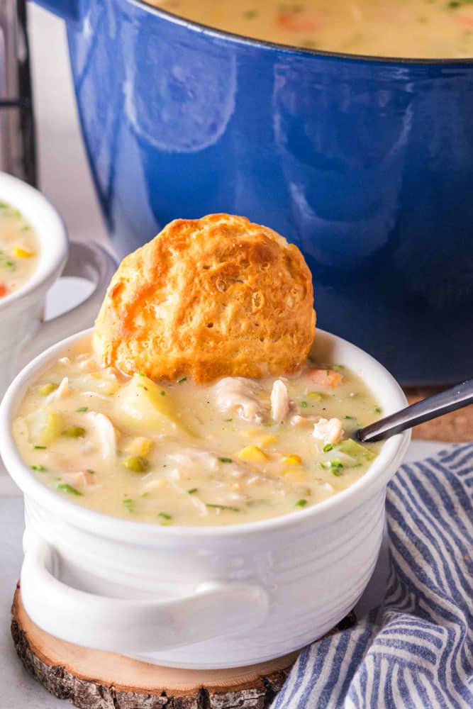 A bowl of chicken pot pie soup with a biscuit on top.