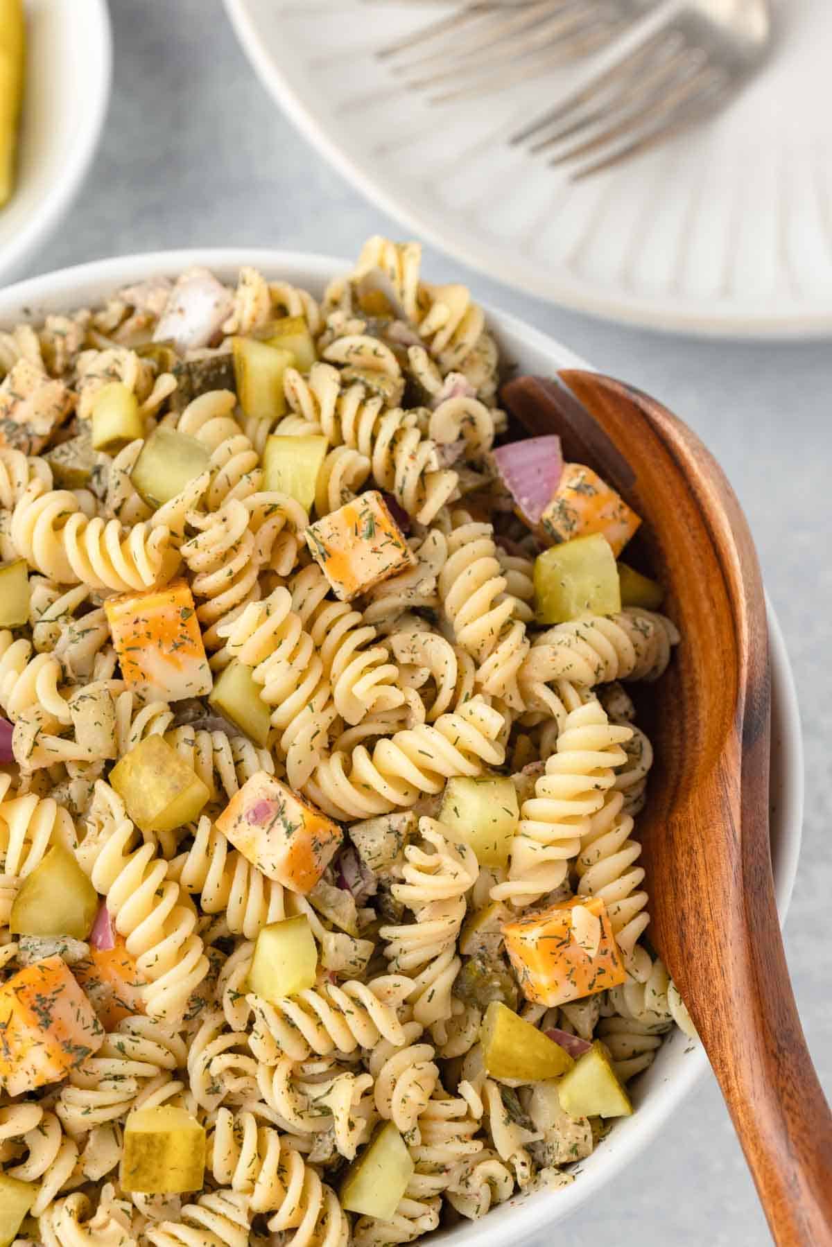 TikTok viral dill pickle pasta salad in a bowl with a wooden spoon.
