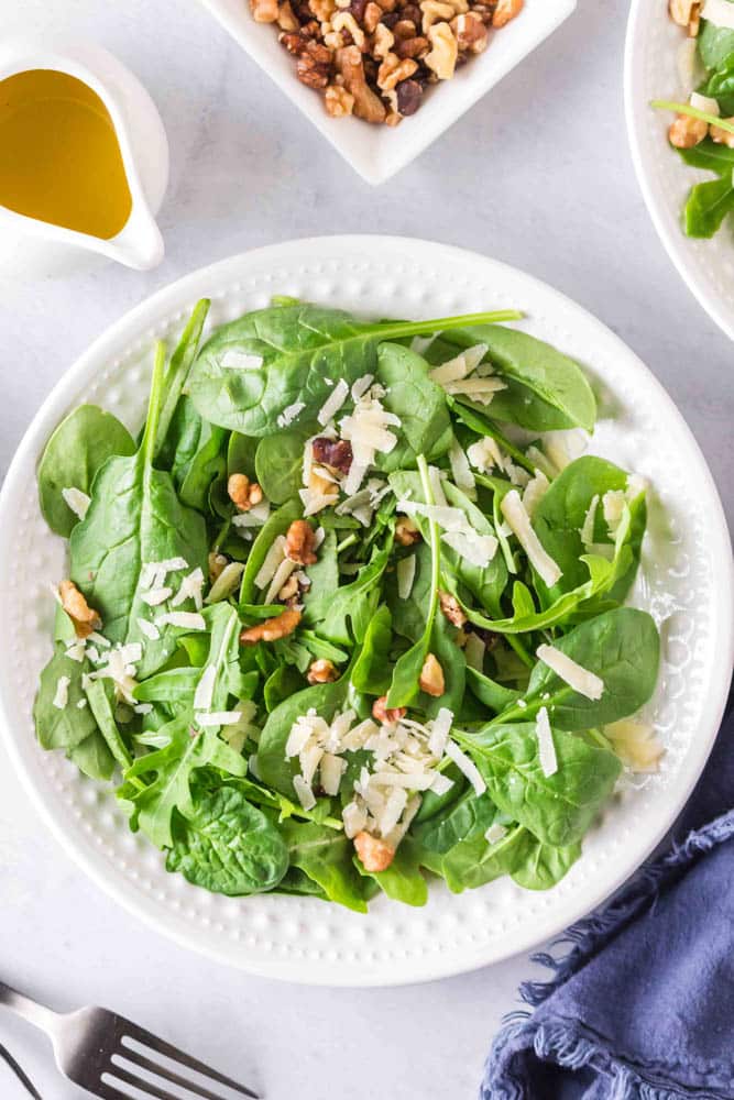 Spinach and arugula along with nuts and cheese on a white plate.