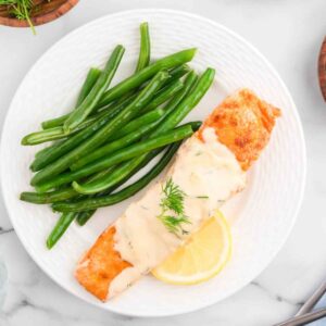 Salmon with dill cream sauce on a plate with green beans.