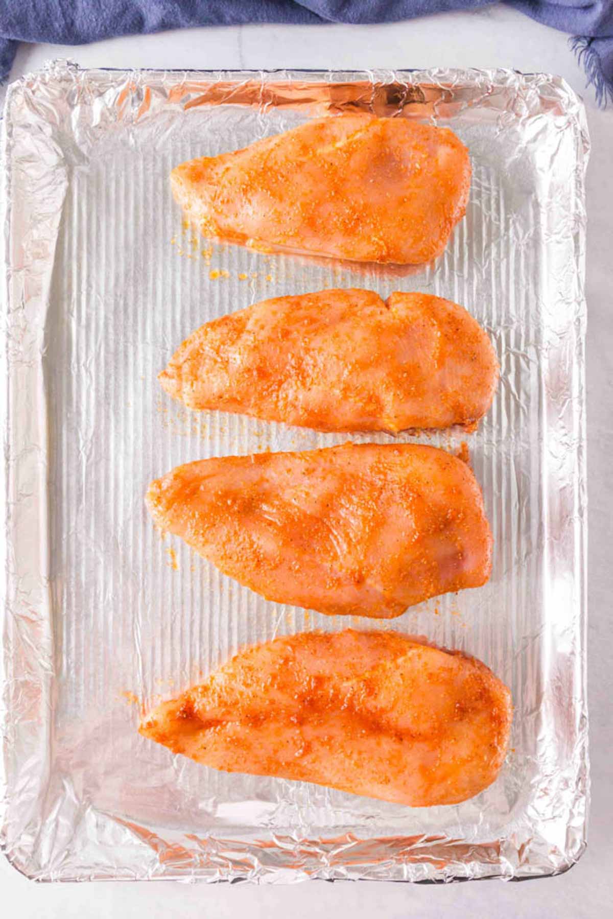 Uncooked chicken breasts on a baking sheet seasoned. 