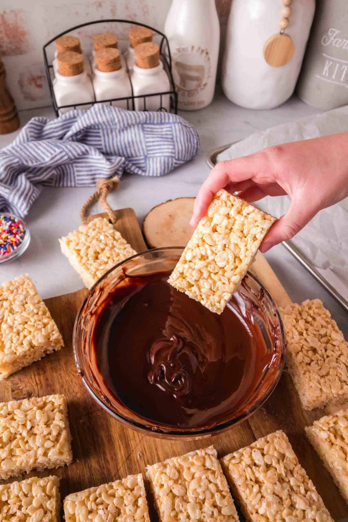 Rice krispie treats being dipped in a bowl of chocolate.