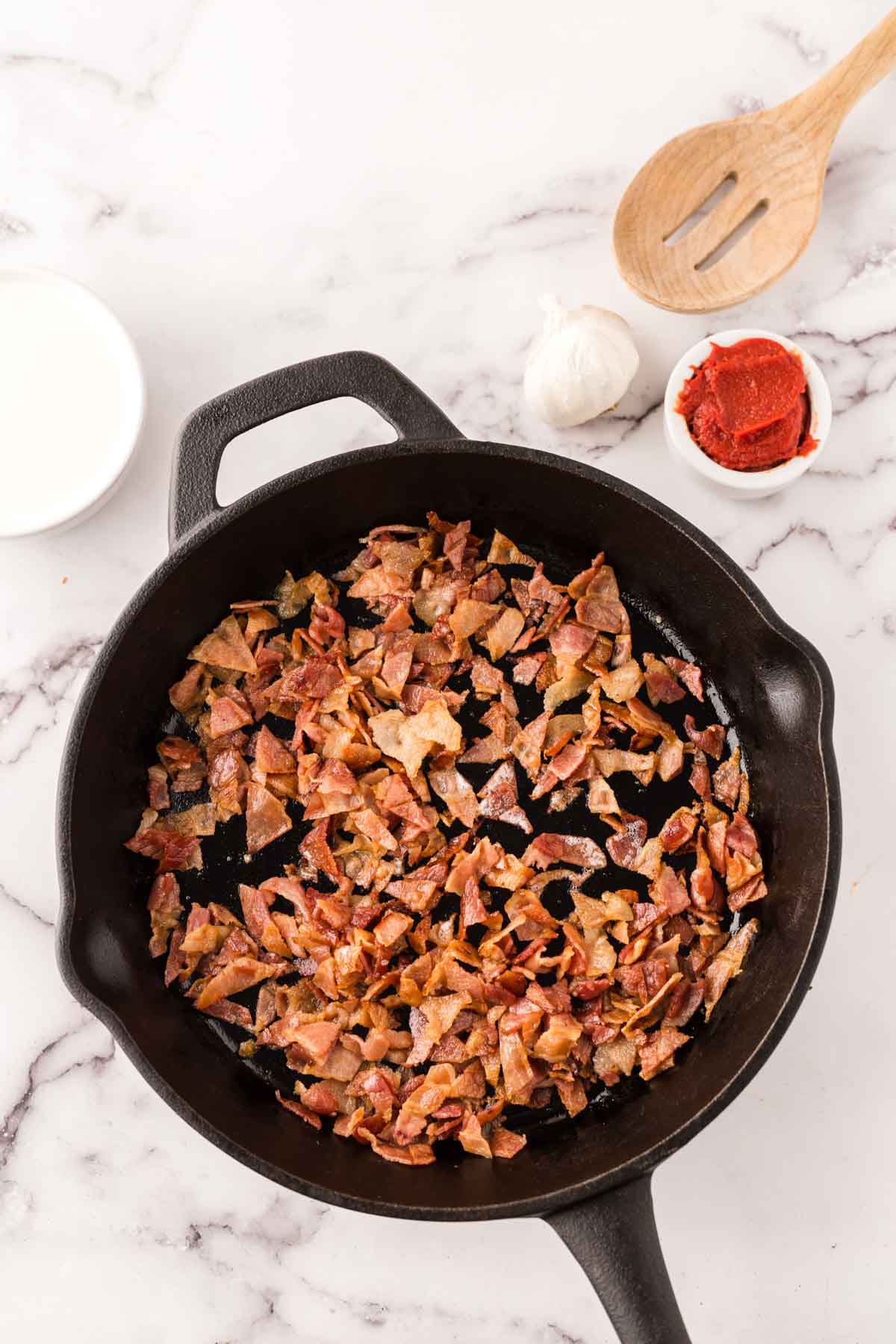 Bacon pieces cooking in a cast iron skillet.