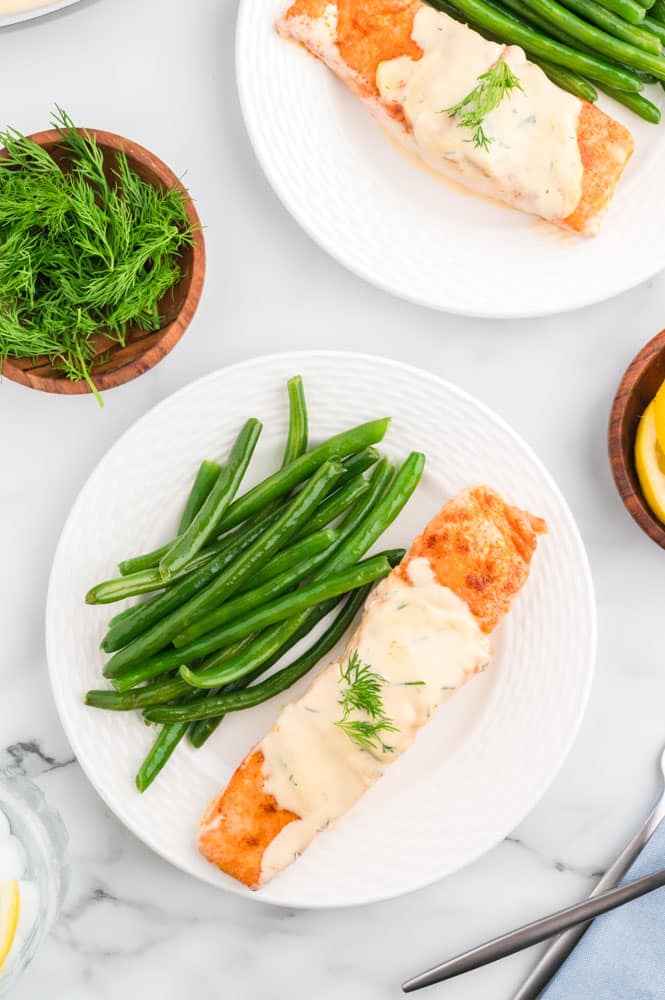 Salmon with dill cream sauce on a white plate with green beans.