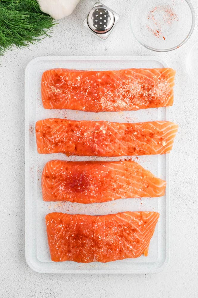 Raw salmon filets on a plate sprinkled with spices.