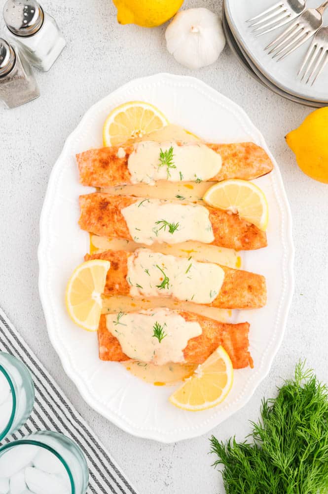 Salmon with Dil Cream Sauce on a white plate garnished with lemon slices.