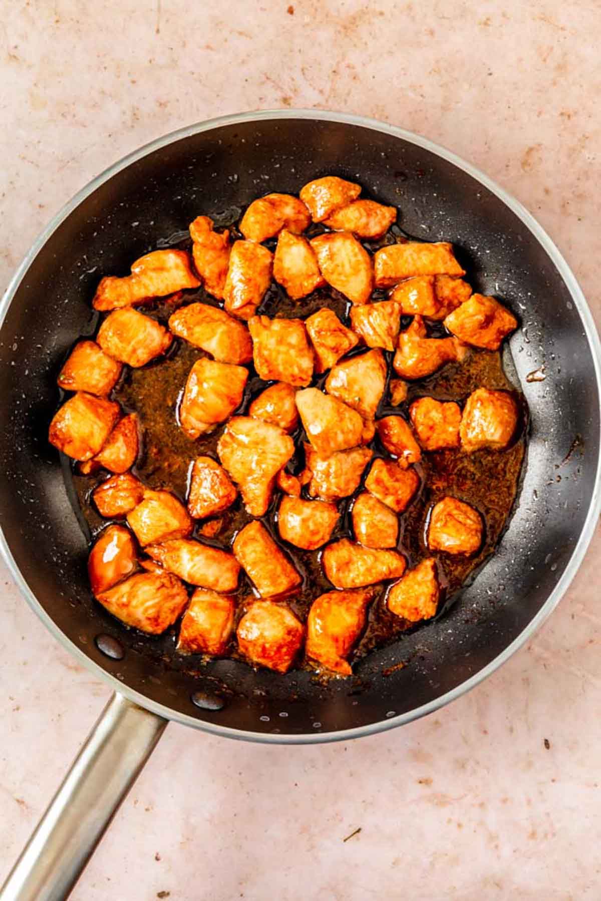 Pieces of chicken cooking in a pan with teriyaki sauce.