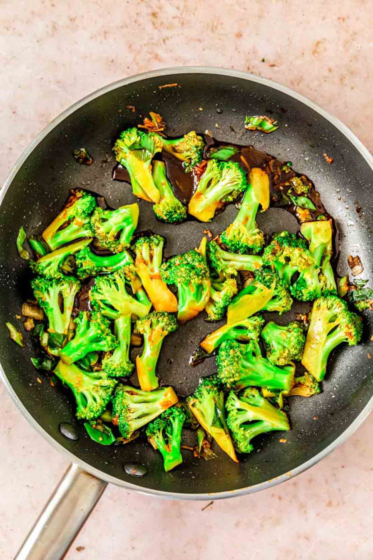 Broccoli cooking in a large skillet with teriyaki sauce.