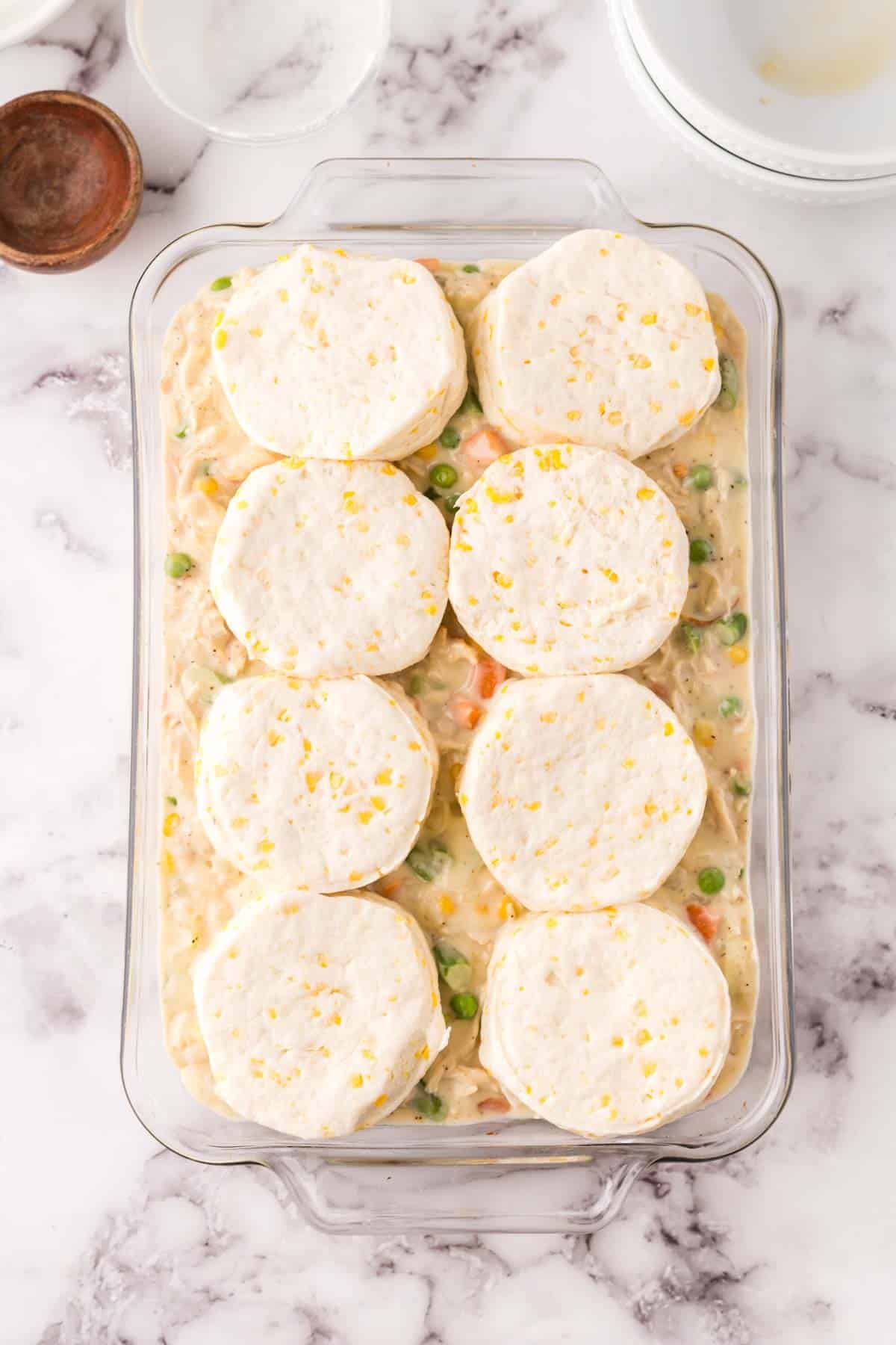 Chicken pot pie casserole topped with raw biscuits ready to bake.