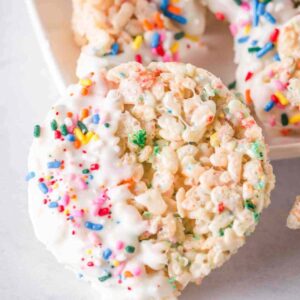 A round rice krispie treat with sprinkles dipped in white chocolate.