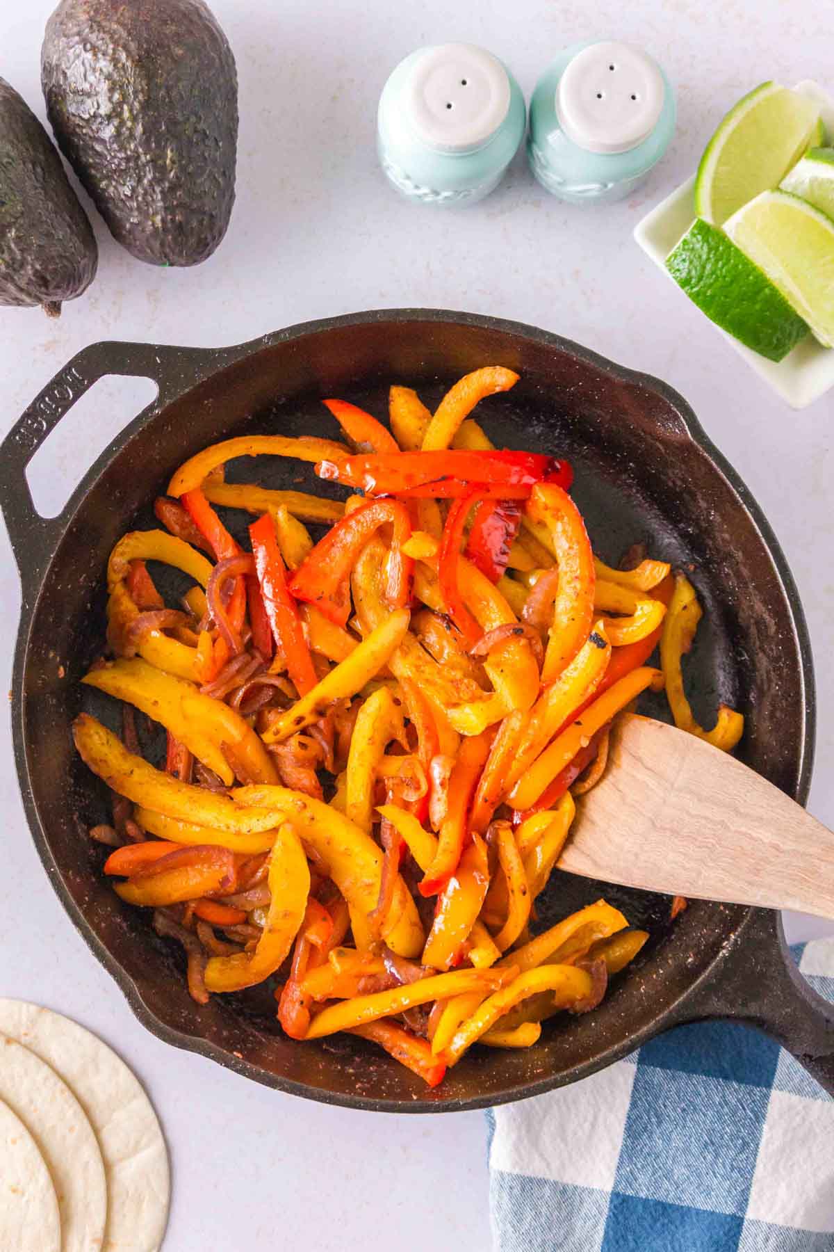 Fajita onions and peppers cooking in a cast iron skillet with a wooden spoon.